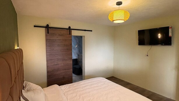 A bedroom with a bed, a TV mounted on the wall, and a wooden door. - Naab Apart Complex (Panajachel)