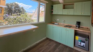 A compact kitchen with a window, green cabinets, a built-in coffee maker, and a refrigerator. - Naab Apart Complex (Panajachel)