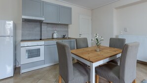 A modern kitchen with grey cabinets, a white refrigerator, and a wooden dining table with four grey upholstered chairs. - Apartment Seralya, Spacious Two Bedroom Apartment, Athens (Athens)