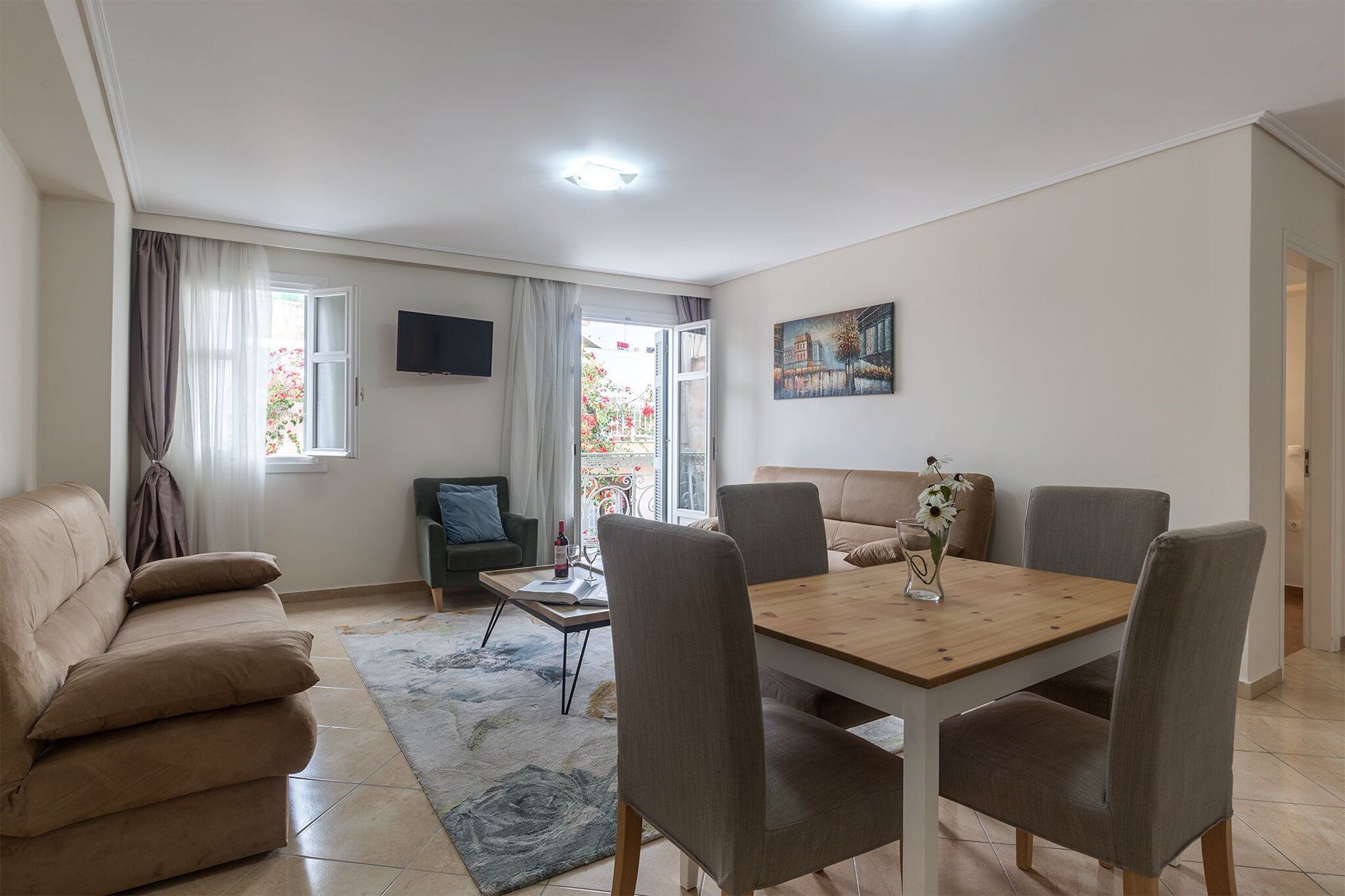 Een woonkamer met een bank, een eettafel met stoelen, een aan de muur bevestigde televisie en een schilderij.