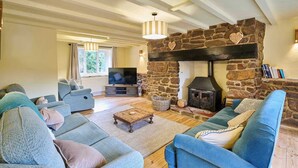 A cozy living room with a stone fireplace, comfortable sofas, a television, and a large window. - Host & Stay | Morley House (Devon)