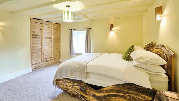 A bedroom with a large bed, wooden headboard, and a unique wooden base. There is a wardrobe and a window with curtains. - Host & Stay | Morley House (Devon)
