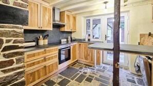 A kitchen with wooden cabinets, a stone wall, and a stone floor. - Host & Stay | Morley House (Devon)
