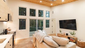 Een moderne woonkamer met een grote televisie, een bank en een keukenhoek met een fornuis.