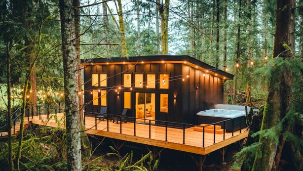 Een chalet met terras, een hottub en lichtjes in een bos.