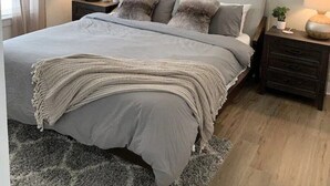 Une chambre à coucher avec un lit, des tables de chevet, un ventilateur de plafond et une fenêtre avec des rideaux.