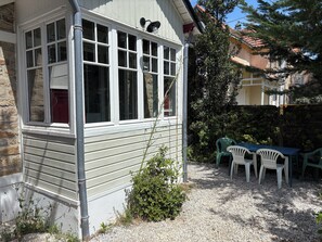 Un bâtiment doté d’une fenêtre, d’une porte et d’un petit espace jardin aménagé avec une table et des chaises.