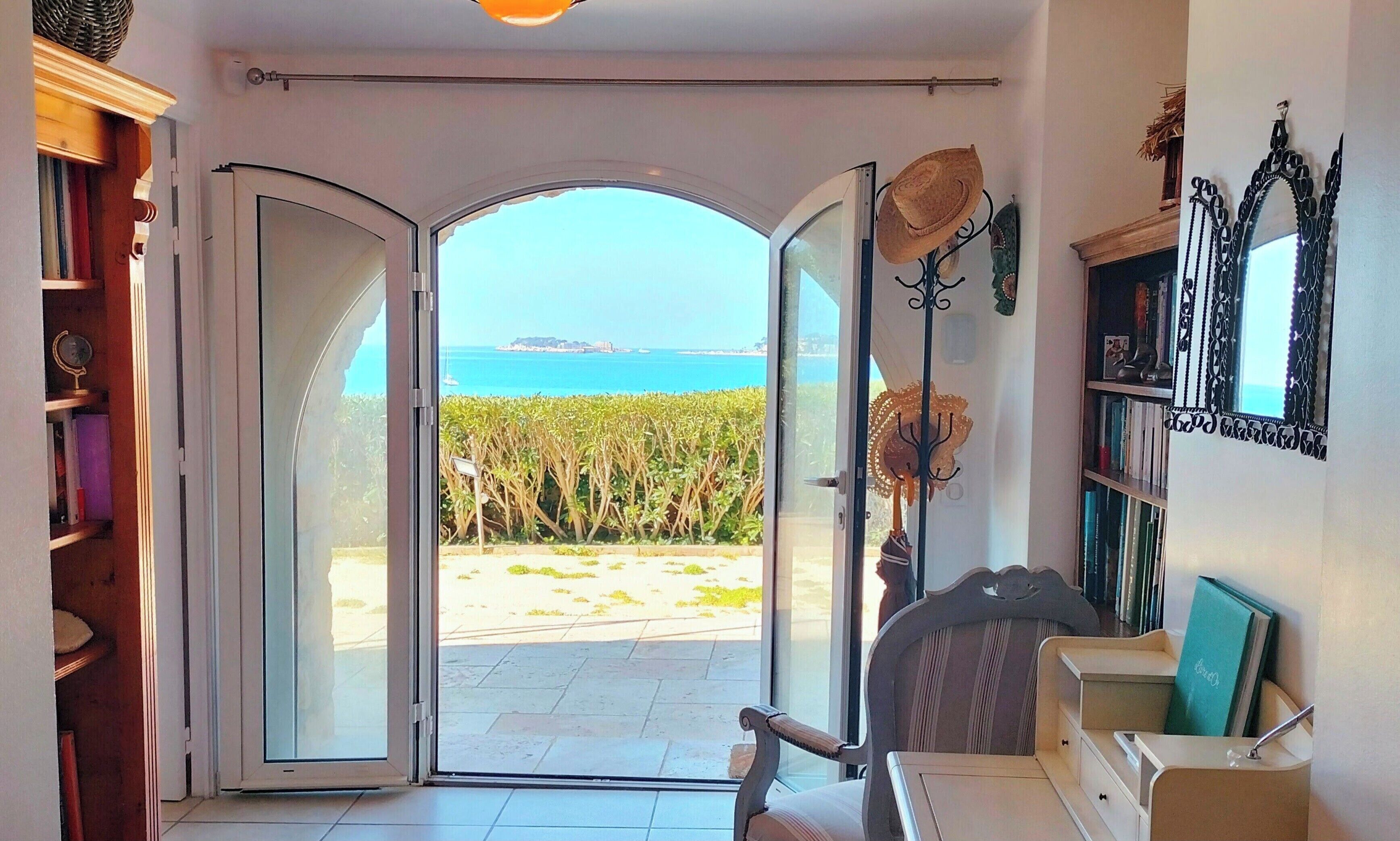 A room with a view of the sea through open doors, a bookshelf, a chair, and a decorative mirror.
