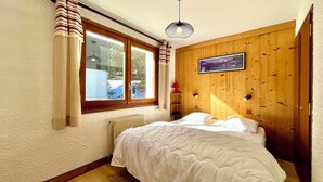 Een slaapkamer met een bed, een raam met gordijnen, een radiator, een houten wand en een foto aan de muur.