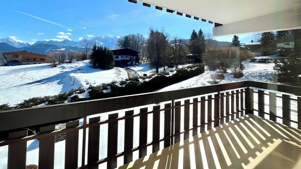 Een balkon met uitzicht op een besneeuwd landschap, een huis en bergen op de achtergrond.