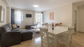 Ett vardagsrum med en grå soffa, ett vitt matbord och en tv som är monterad på väggen.
