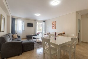 Ein Wohnzimmer mit grauem Sofa, weißem Esstisch und einem an der Wand montierten Fernseher.