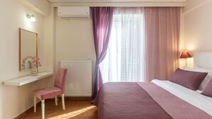 Ett hotellrum med en säng, en stol, en sminkbord med spegel och ett fönster med gardiner.