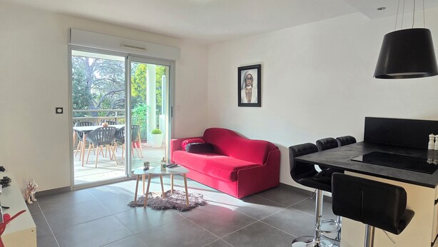A modern living room with a red sofa, a dining table, and a kitchen area. - Saint-Raphaël: Apartment Near Beach & Pool (Saint-Raphaël)