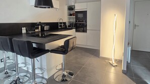 A modern kitchen with a black countertop, three bar stools, a built-in oven, and a pendant light. - Saint-Raphaël: Apartment Near Beach & Pool (Saint-Raphaël)