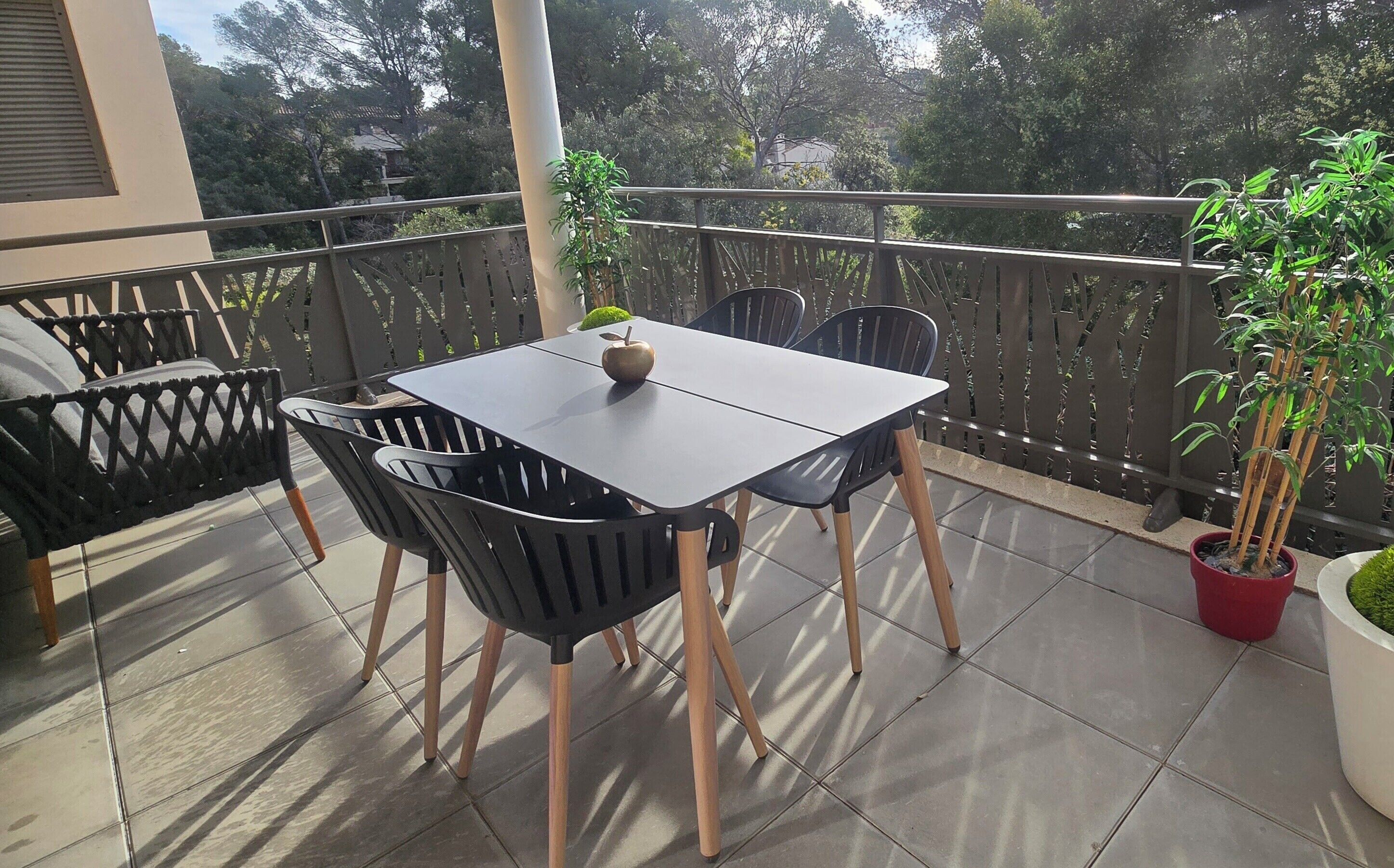 A balcony with a table and chairs, a potted plant, and a view of trees and buildings.