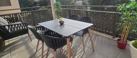 A balcony with a table and chairs, a potted plant, and a view of trees and buildings.