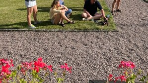 Un grupo de personas al aire libre cerca de un lago, con un camino de grava y vegetación.