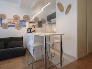 Eine moderne Küche mit weißer Arbeitsplatte, Barhocker und einem eingebauten Ofen. Auf der Arbeitsplatte befindet sich eine Couch und eine Kaffeemaschine.