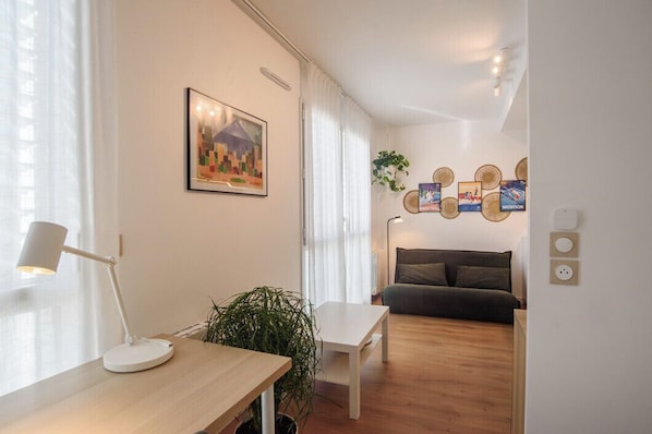 Ein modernes Wohnzimmer mit einer Couch, einem Tisch mit Lampe, einer Topfpflanze und einer Wand mit gerahmten Bildern.