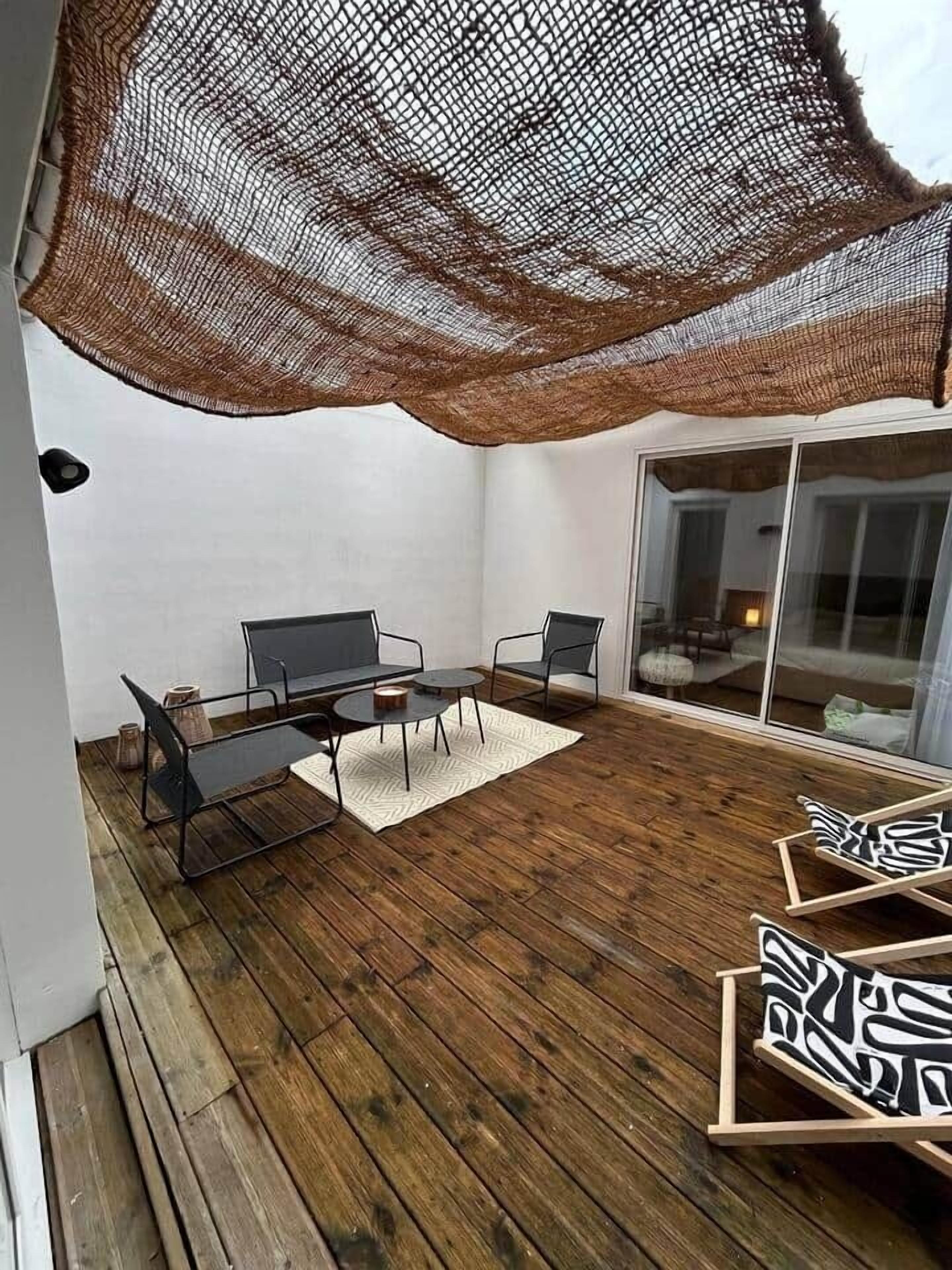 Une terrasse dotée d’une plateforme en bois, de deux chaises en métal noir, d’une petite table ronde et d’un parasol en fibres tressées.