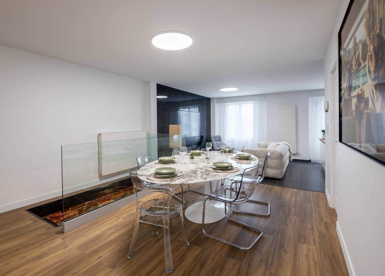Een moderne eethoek met een ronde tafel, transparante stoelen en een glazen scheidingswand.