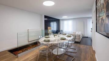 Een moderne eethoek met een ronde tafel, transparante stoelen en een glazen scheidingswand.