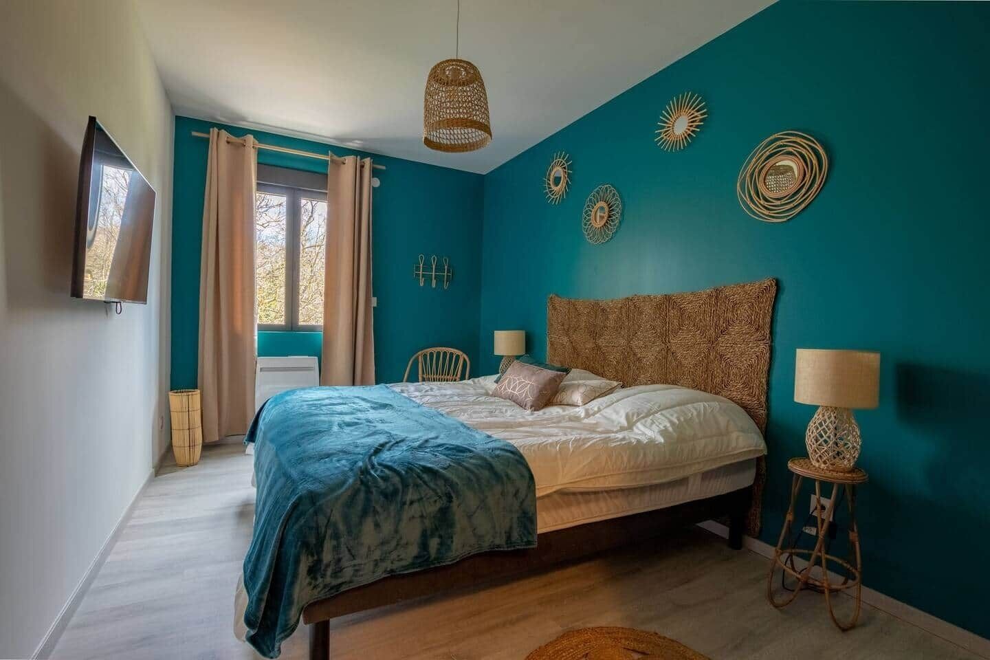 A bedroom with teal walls, a wooden bed, a TV, and decorative wall art.