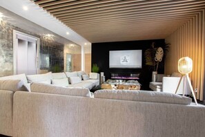 A modern living room with a large sectional sofa, a flat-screen TV mounted on the wall, and a unique wooden ceiling design.