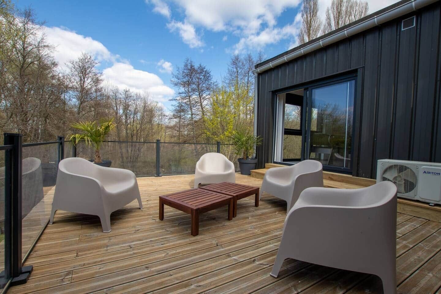 A modern outdoor deck with wooden flooring, white plastic chairs, and a wooden table.