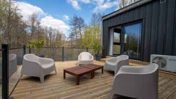 A modern outdoor deck with wooden flooring, white plastic chairs, and a wooden table.