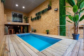 An indoor swimming pool with wooden decking, surrounded by walls with vertical gardens and a green artificial grass wall.