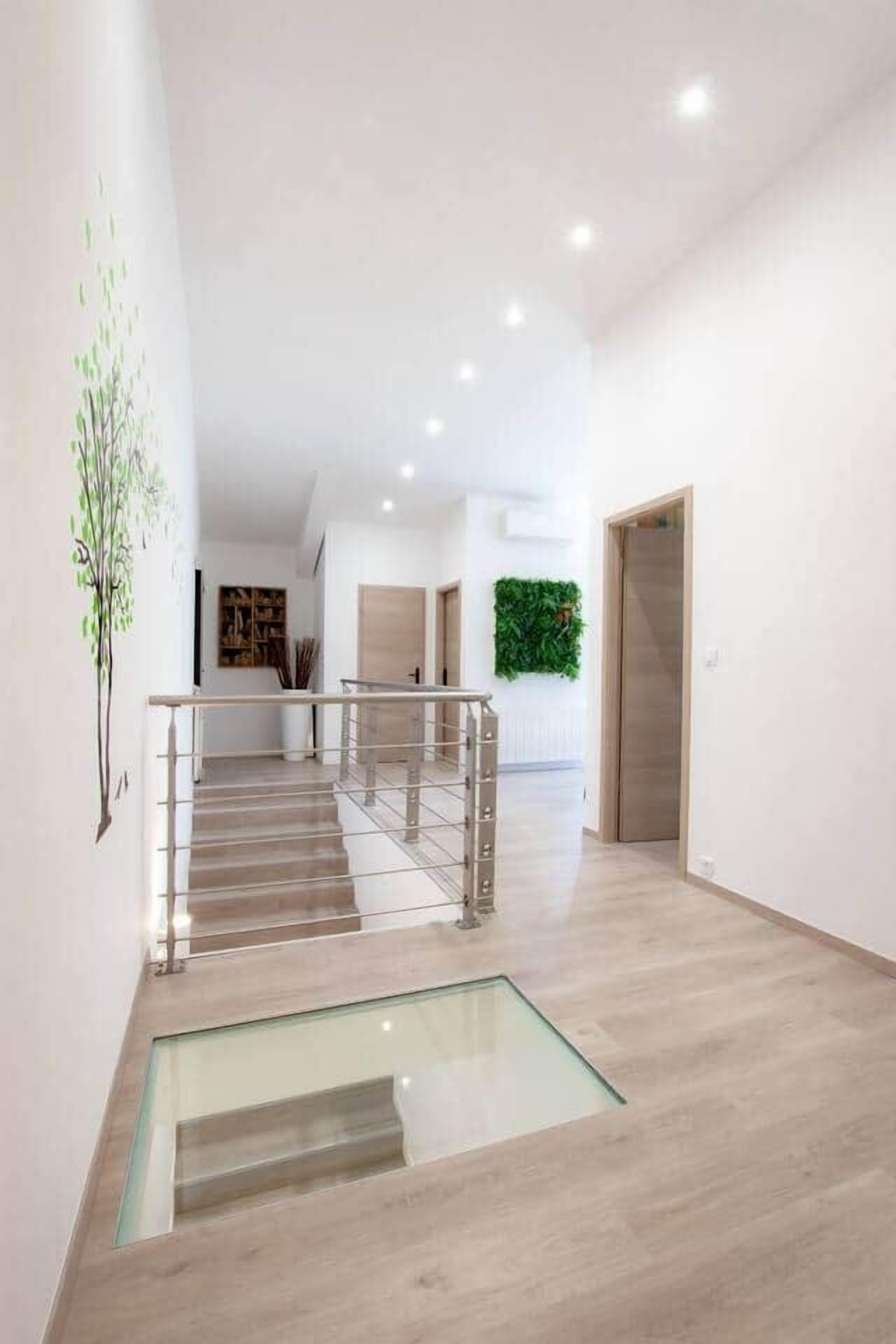 A modern interior with a glass-bottomed staircase leading to a second floor, white walls, and a green wall decoration.