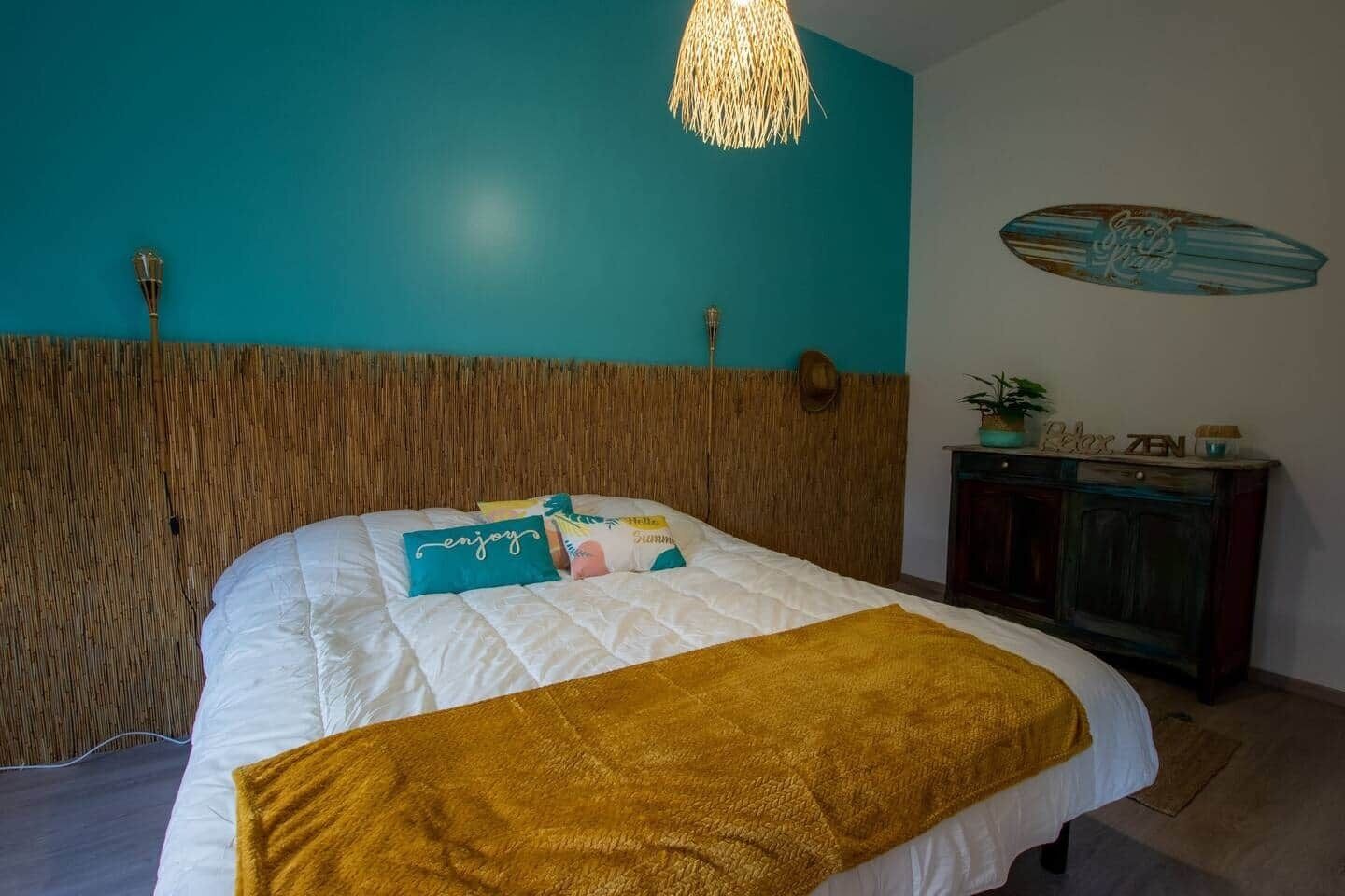 Une chambre à coucher comprenant un lit, une tête de lit, une table de chevet, une décoration sur le thème du surf et un luminaire suspendu.