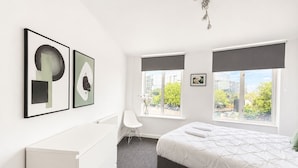 Un dormitorio moderno con cama, un aparador blanco, una silla y una obra de arte en la pared.