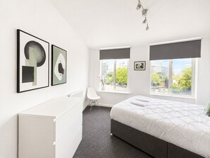 Ein modernes Schlafzimmer mit einem Bett, einer weißen Kommode, einem Stuhl und Kunstwerken an der Wand.