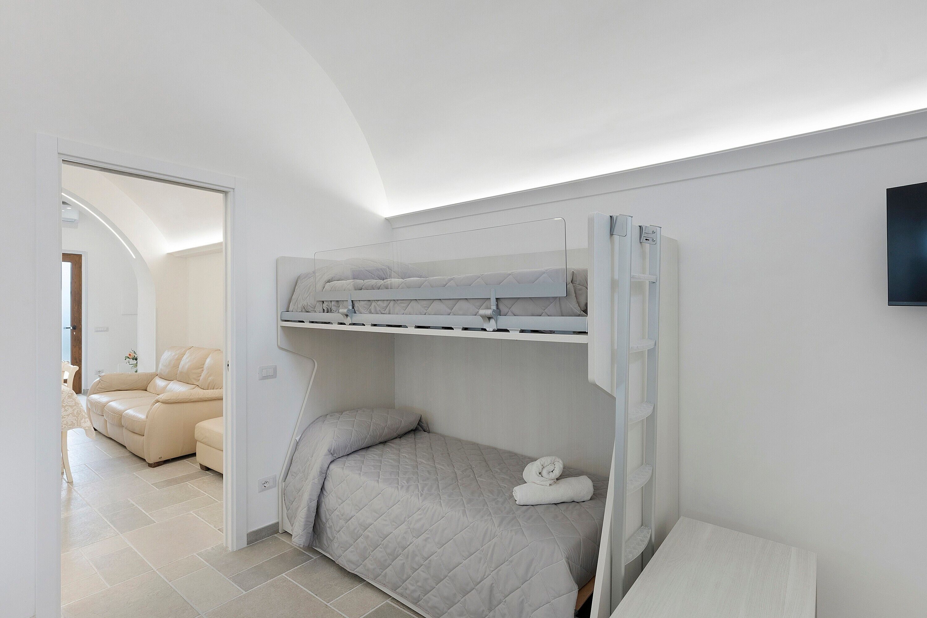 A bedroom with a bunk bed, a flat-screen TV, a bedside table, and a sofa in the adjacent living area.