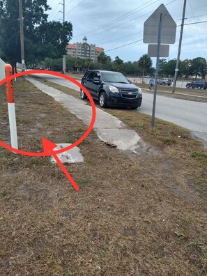 Un SUV negro estacionado en la banquina de una calle con césped, con una señal de alto y un edificio al fondo.