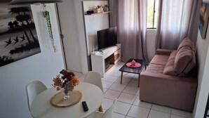 Ein Wohnzimmer mit Sofa, Fernseher und einem Esstisch mit Stühlen.