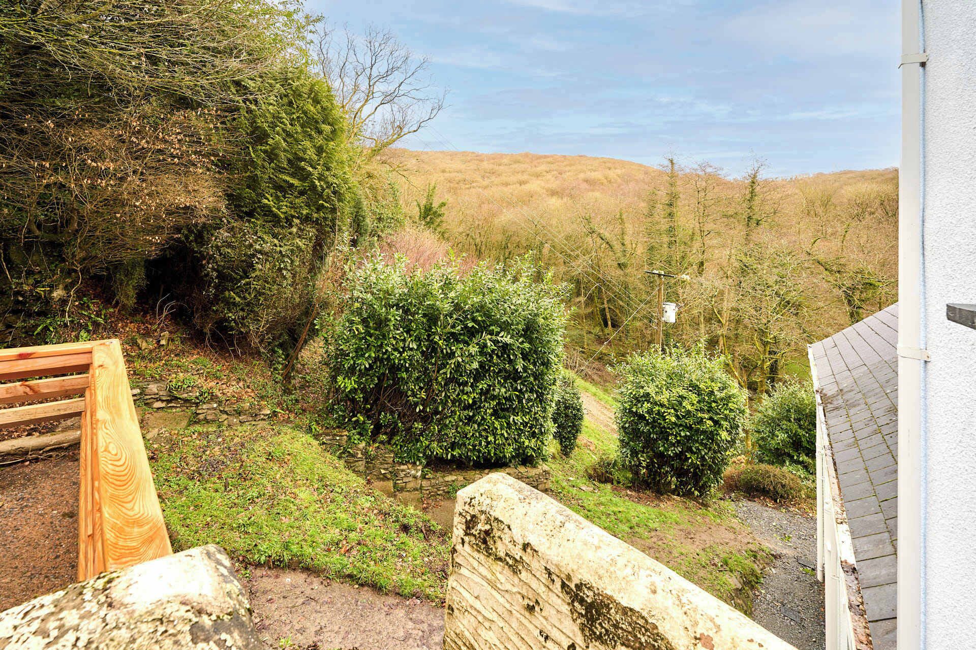 Un jardin avec un banc en bois, un mur de pierre et une vue sur les collines.