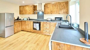 A modern kitchen with wooden cabinets, stainless steel appliances, and a large island with a sink. - Host & Stay | Morley Cottage (Devon)