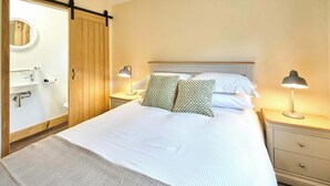 A bedroom with a bed, two bedside tables with lamps, a wooden wardrobe, a round mirror, and a white sink. - Host & Stay | Morley Cottage (Devon)