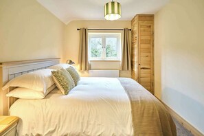 A neatly made bed with striped bedding and decorative pillows, a bedside lamp, a window with curtains, and a wooden wardrobe.