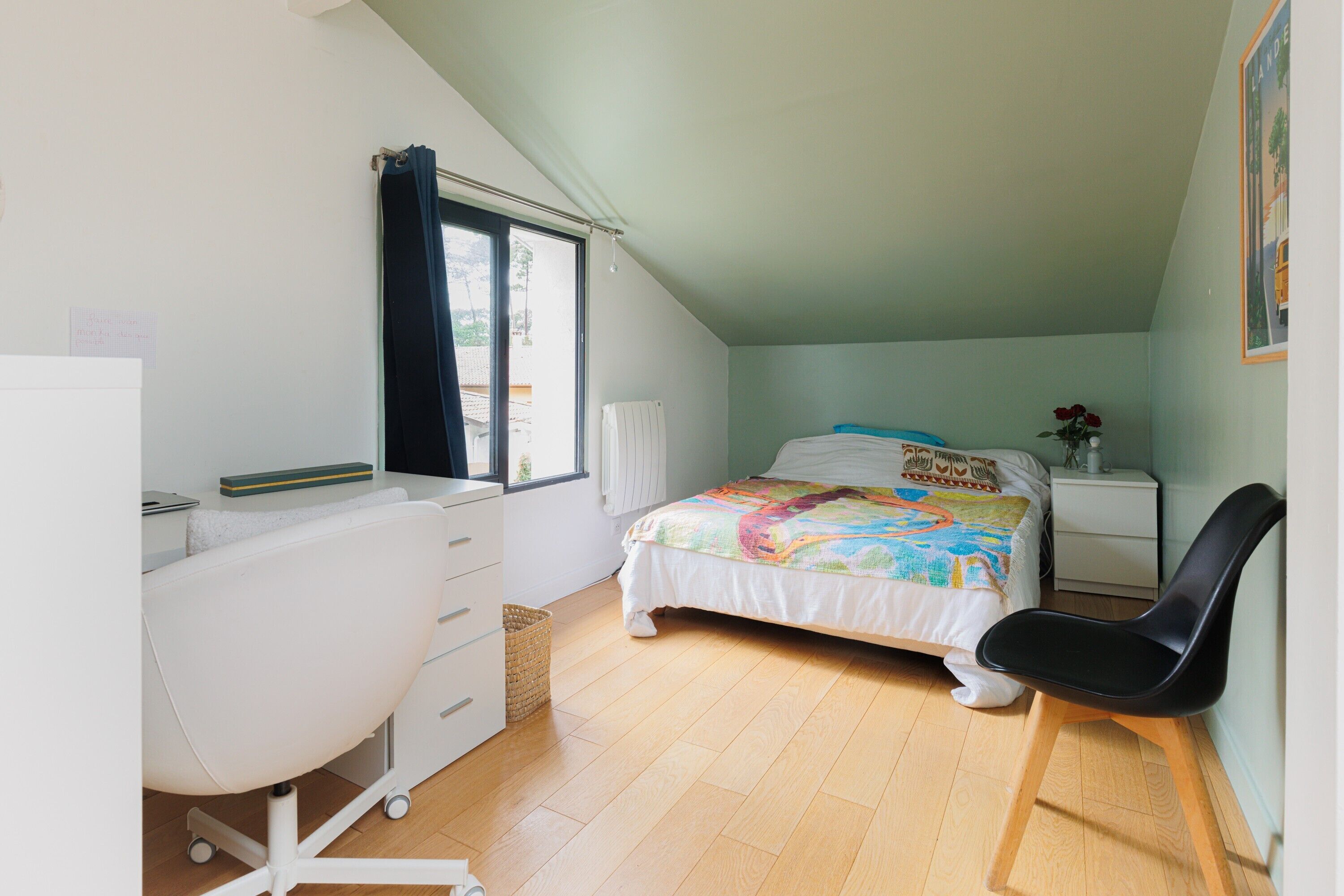 Ein Schlafzimmer mit Bett, Schreibtisch, Stuhl, Fenster und Nachttisch.