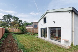 A modern house with a large glass door, a small patio table, and a wooden fence in the background. - Villa "Dacapa" with Private Terrace, Garden, and Wi-Fi (Capbreton)