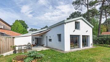 Una casa moderna con fachada blanca, techo inclinado y un patio cubierto.