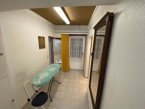 Een kamer met een bed, nachtkastje, stoel, raam met gele gordijnen en een spiegel aan de muur.