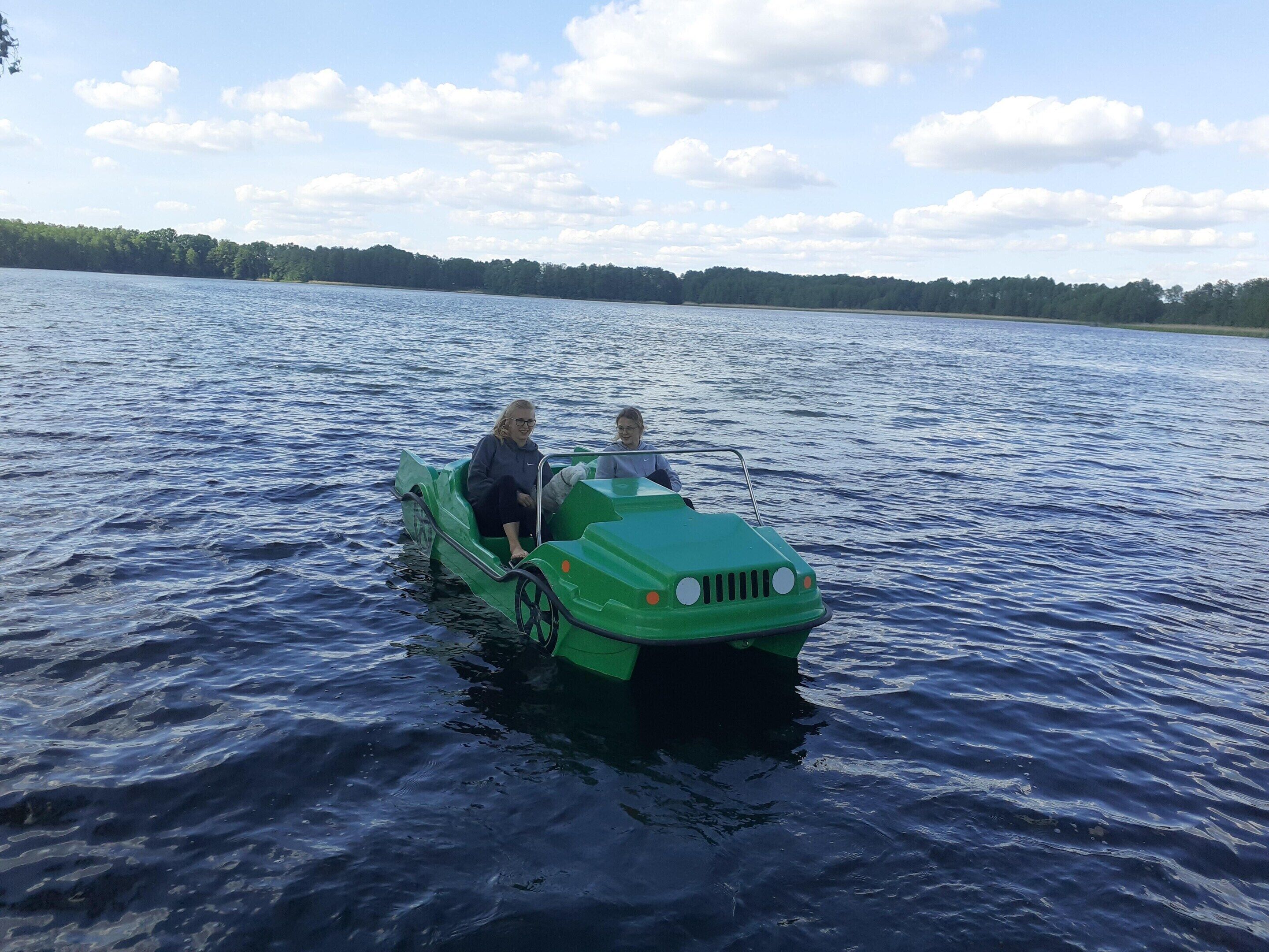 A green boat on a lake with two people on board.
