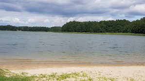 A lake with a sandy beach and a forested area in the background. - Large House With Private Garden, Right on the Lake (Lubrza)