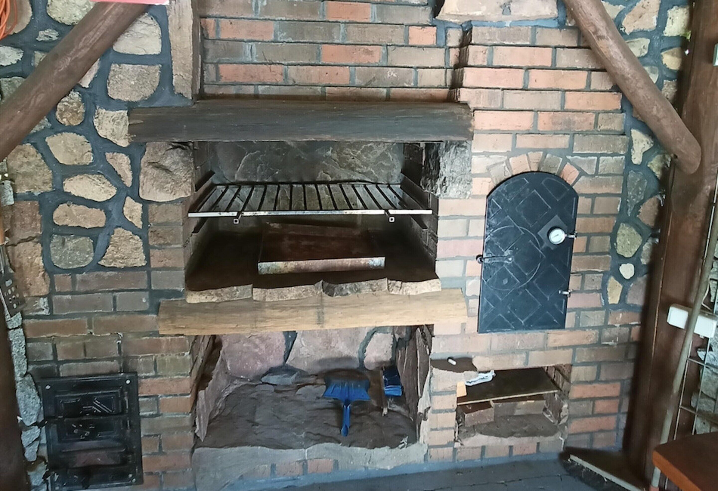 A stone and brick fireplace with a wooden shelf above it and a small door to the right.